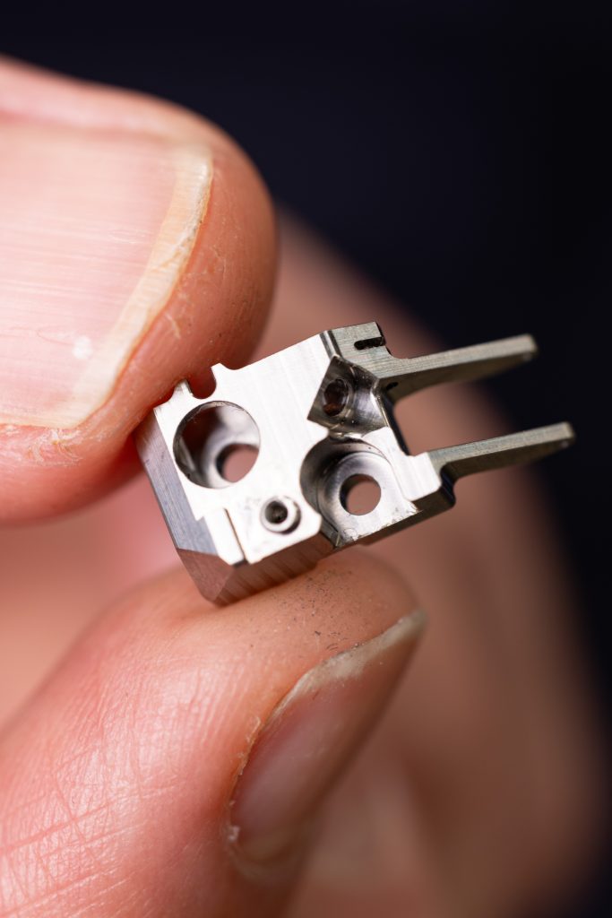 Pièce métallique miniature micro-usinée sur machine KERN, tenue entre les doigts, illustrant le savoir-faire Chastagner en micro-mécanique et mécanique de précision.